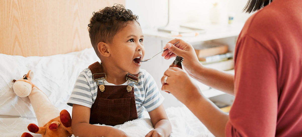 Parent giving child liquid medicine with spoon during at-home pediatric medication administration